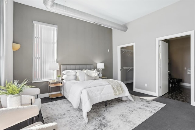 bedroom featuring dark colored carpet, a closet, a spacious closet, and baseboards