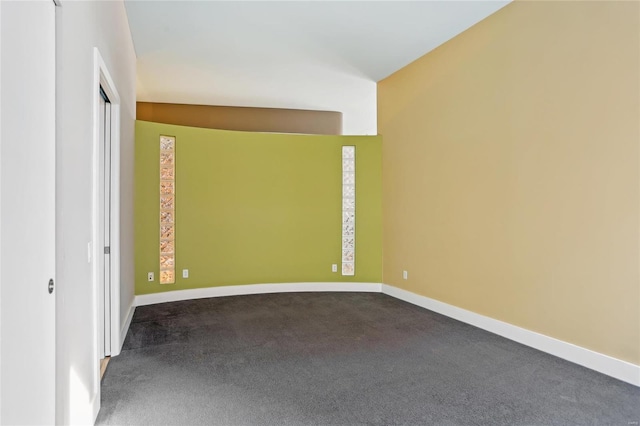 empty room featuring dark colored carpet and baseboards