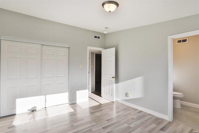 unfurnished bedroom with light wood-type flooring, ensuite bathroom, and a closet