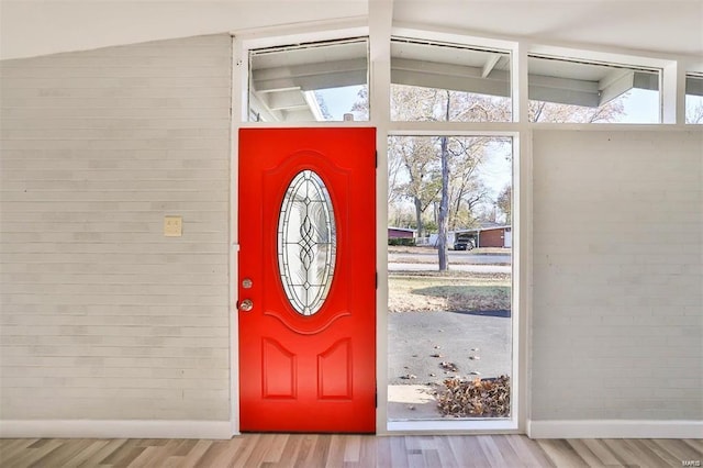 entrance foyer with light hardwood / wood-style floors, vaulted ceiling, and brick wall