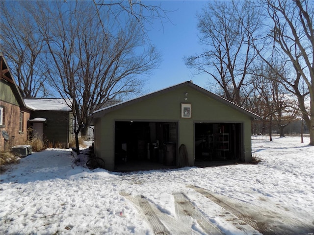 snow covered house with a garage and an outdoor structure