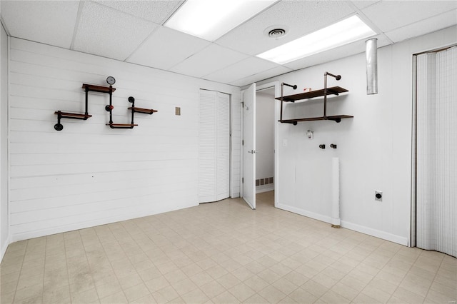 basement with a drop ceiling and wood walls