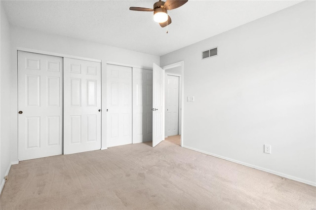 unfurnished bedroom featuring ceiling fan, light colored carpet, a textured ceiling, and two closets