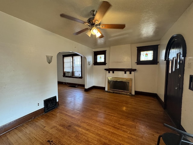 unfurnished living room with a textured ceiling, ceiling fan, a wealth of natural light, and dark wood-type flooring