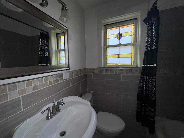 bathroom featuring tile walls, curtained shower, sink, and toilet