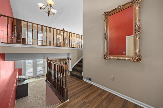 stairway featuring a textured ceiling, an inviting chandelier, and wood-type flooring