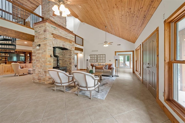 living room featuring a wood stove, wood ceiling, high vaulted ceiling, ceiling fan, and light tile patterned flooring