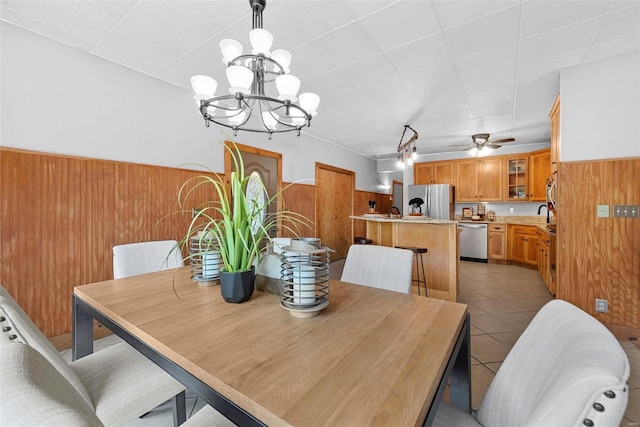 dining room featuring light tile patterned floors, ceiling fan with notable chandelier, and wooden walls