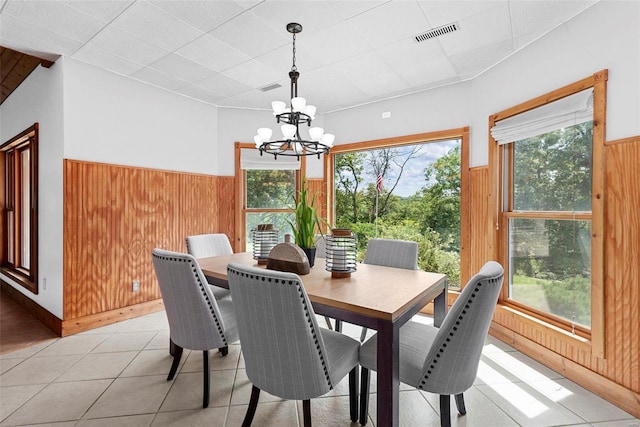 dining area with wooden walls, a chandelier, and light tile patterned flooring