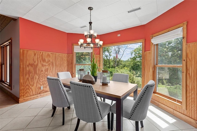 dining area with an inviting chandelier, wooden walls, and a healthy amount of sunlight