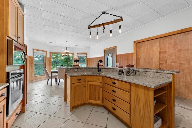 kitchen with sink, appliances with stainless steel finishes, a kitchen island with sink, hanging light fixtures, and light stone counters