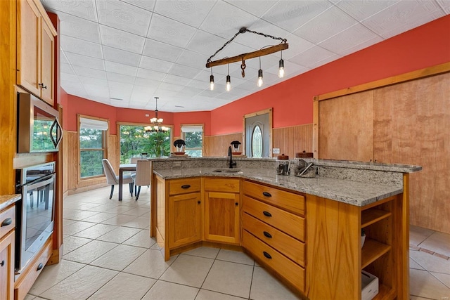 kitchen with sink, an inviting chandelier, light stone counters, pendant lighting, and stainless steel appliances