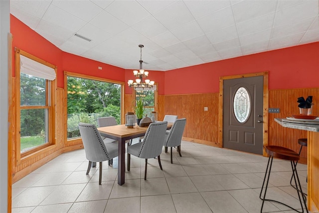 dining area with light tile patterned floors, a notable chandelier, and wood walls