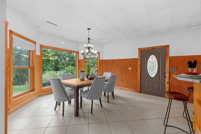 dining space with light tile patterned flooring, a chandelier, and wood walls