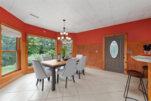 dining area with light tile patterned flooring, wooden walls, and a chandelier