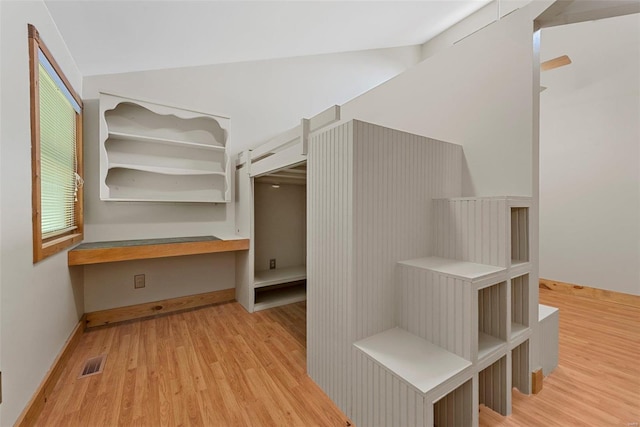 spacious closet with lofted ceiling, built in desk, and light hardwood / wood-style floors