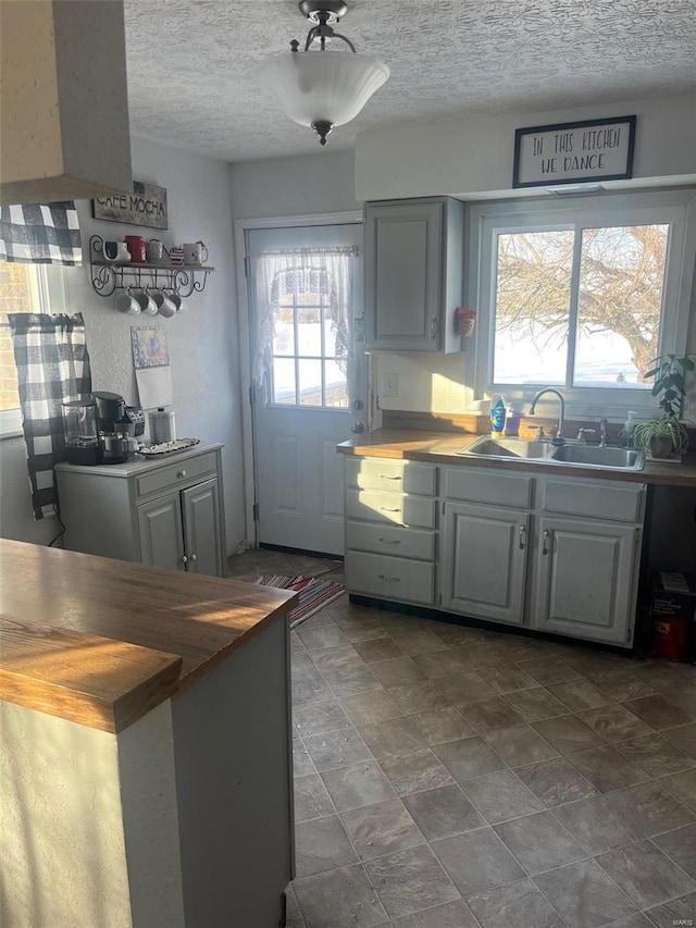 kitchen featuring sink, butcher block countertops, a textured ceiling, and gray cabinetry