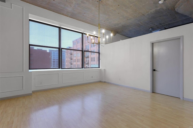 spare room featuring plenty of natural light, light hardwood / wood-style flooring, and a notable chandelier