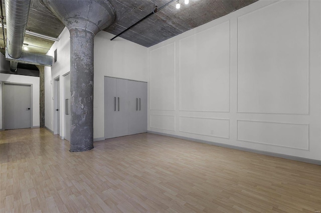 empty room with a towering ceiling, ornate columns, and light hardwood / wood-style flooring