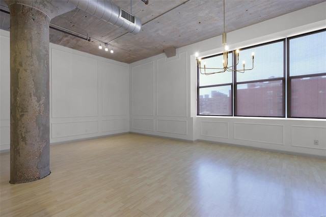 spare room featuring a notable chandelier, light hardwood / wood-style floors, and decorative columns