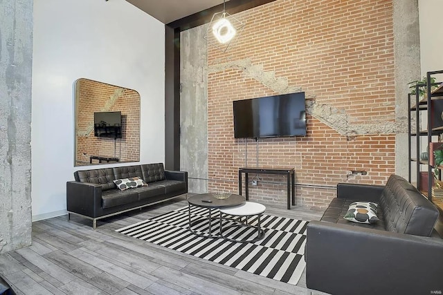 living room with a high ceiling, brick wall, and light hardwood / wood-style flooring