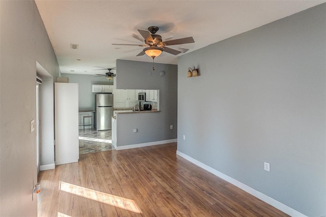 unfurnished living room with ceiling fan, sink, and light hardwood / wood-style flooring