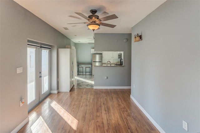 unfurnished living room with french doors, ceiling fan, sink, and light hardwood / wood-style flooring