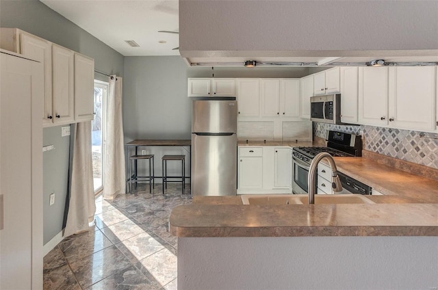 kitchen with stainless steel appliances, decorative backsplash, white cabinets, and kitchen peninsula