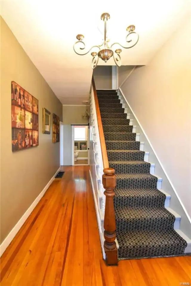 stairway featuring a notable chandelier, baseboards, and wood finished floors