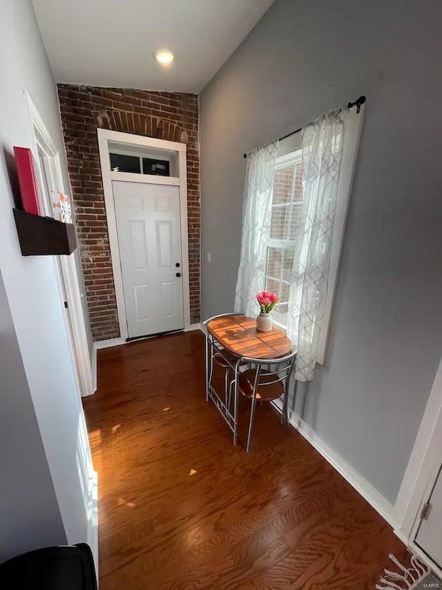 hallway featuring wood finished floors, baseboards, and brick wall