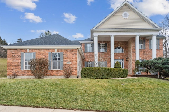 neoclassical home with a shingled roof, brick siding, and a front lawn