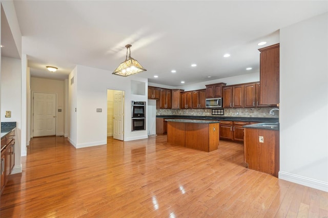 kitchen with tasteful backsplash, dark countertops, light wood-style flooring, a kitchen island, and appliances with stainless steel finishes