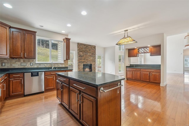 kitchen featuring a center island, light wood-style floors, a sink, a stone fireplace, and dishwasher