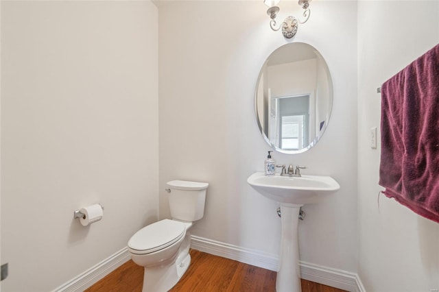 half bath with baseboards, a sink, toilet, and wood finished floors