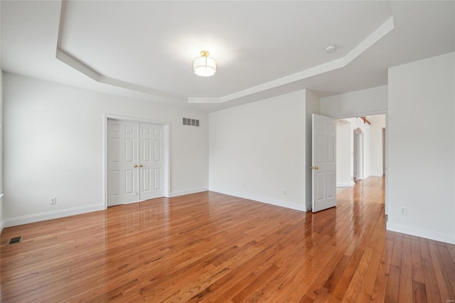 empty room with visible vents, arched walkways, a raised ceiling, baseboards, and light wood-style floors