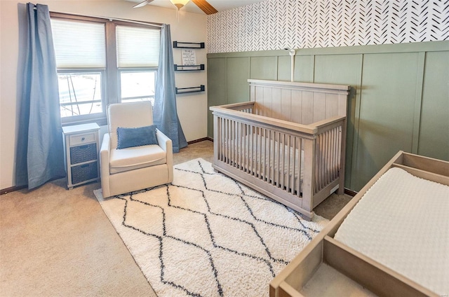 carpeted bedroom featuring ceiling fan and a nursery area