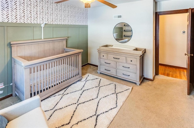 carpeted bedroom featuring ceiling fan and a nursery area