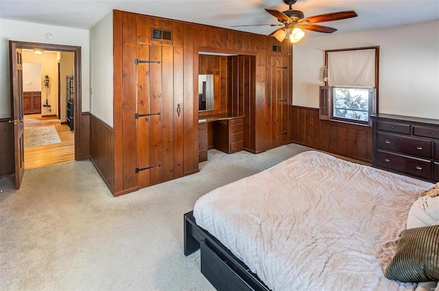 carpeted bedroom with ceiling fan, wooden walls, and connected bathroom