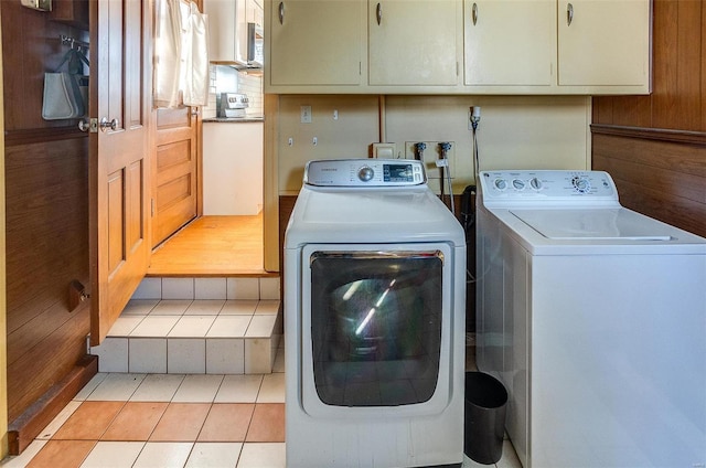 washroom featuring light tile patterned floors, cabinets, washer and dryer, and wood walls