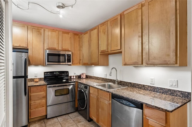 kitchen featuring washer / clothes dryer, stainless steel appliances, light tile patterned floors, dark stone counters, and sink