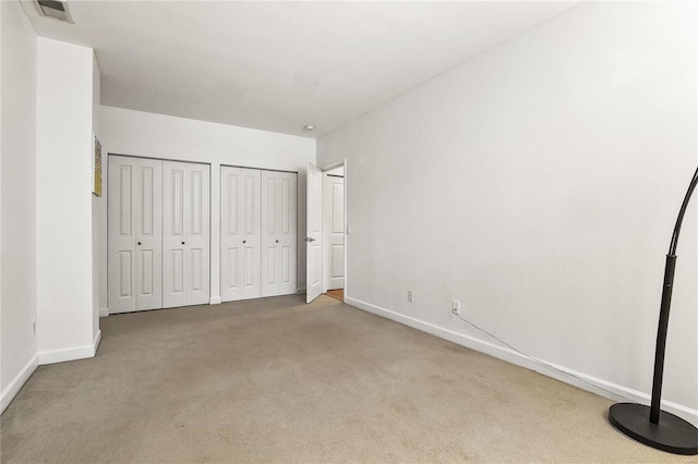 unfurnished bedroom with multiple closets and light colored carpet