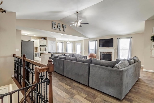 living room featuring high vaulted ceiling, a fireplace, baseboards, light wood-style floors, and an inviting chandelier