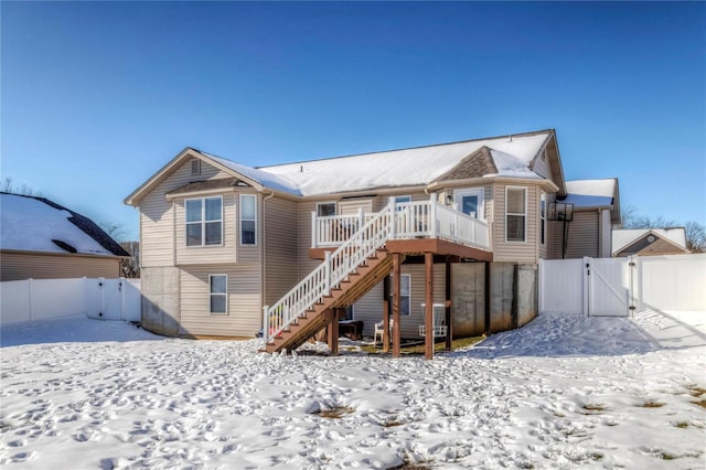 snow covered rear of property with a gate, fence, a wooden deck, and stairs