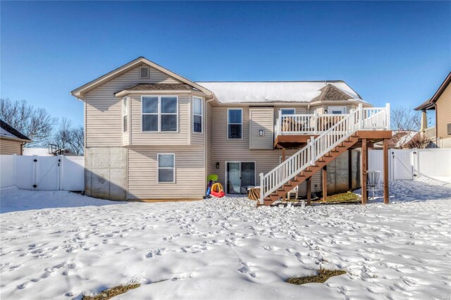 snow covered house with a gate, stairway, fence, and a wooden deck