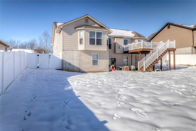 snow covered back of property featuring a gate, fence, a deck, and stairs