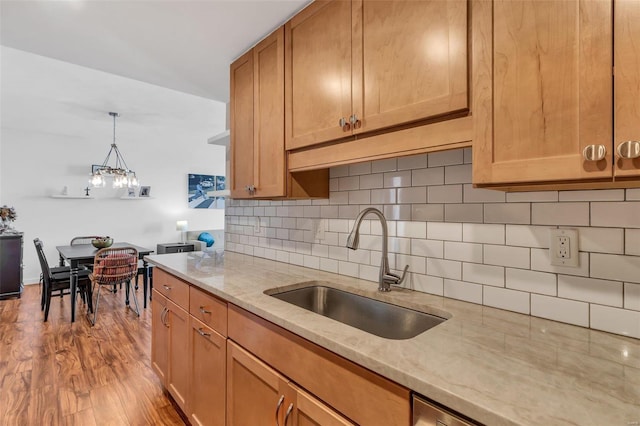 kitchen with light stone countertops, pendant lighting, decorative backsplash, sink, and light hardwood / wood-style flooring