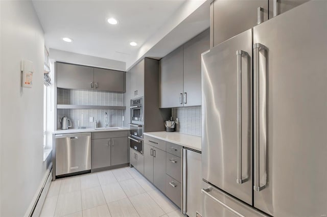 kitchen featuring light countertops, baseboard heating, gray cabinets, stainless steel appliances, and a sink