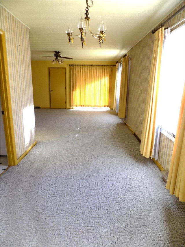 carpeted spare room with ceiling fan with notable chandelier