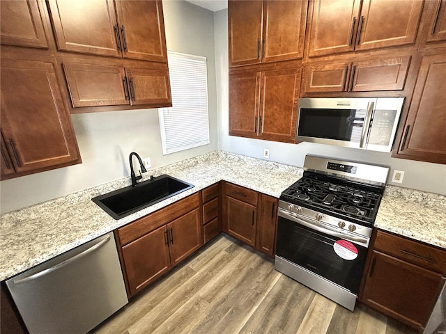 kitchen with appliances with stainless steel finishes, light hardwood / wood-style flooring, light stone counters, and sink