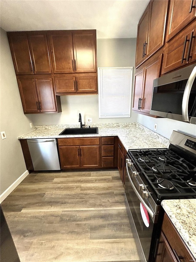 kitchen with light stone countertops, sink, wood-type flooring, and appliances with stainless steel finishes